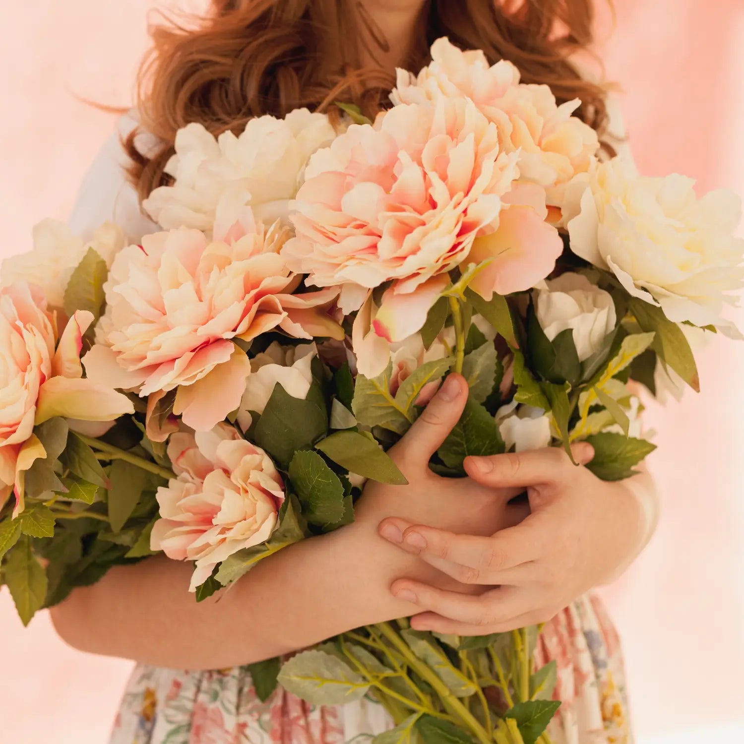 Bouquet of pink and white flowers held by a person with a soft pink background