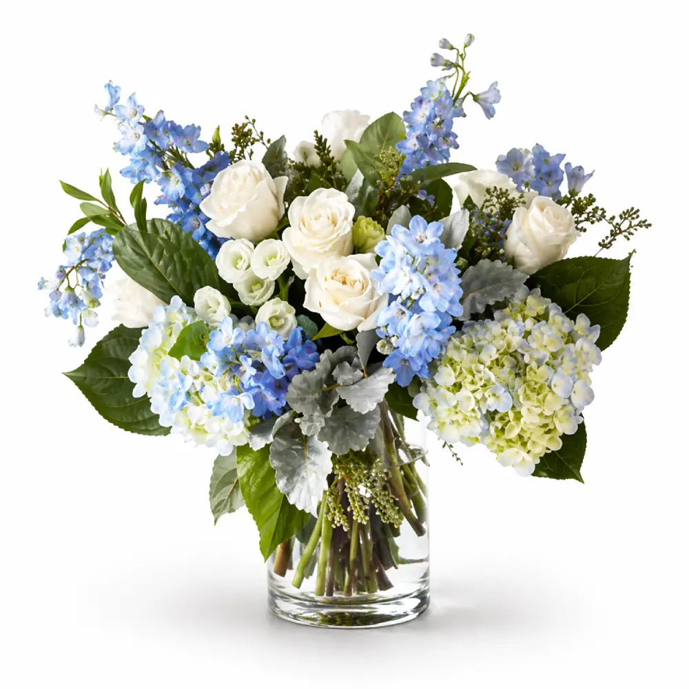 Bouquet of white and blue flowers in a clear vase on a white background