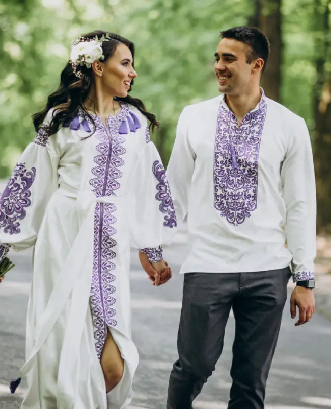 Couple in traditional embroidered clothing walking outdoors with greenery in the background