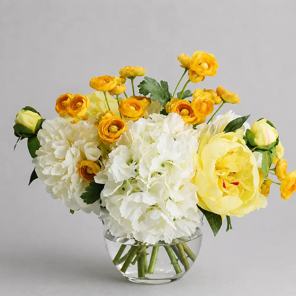 Bouquet of yellow and white flowers in a clear vase on a gray background