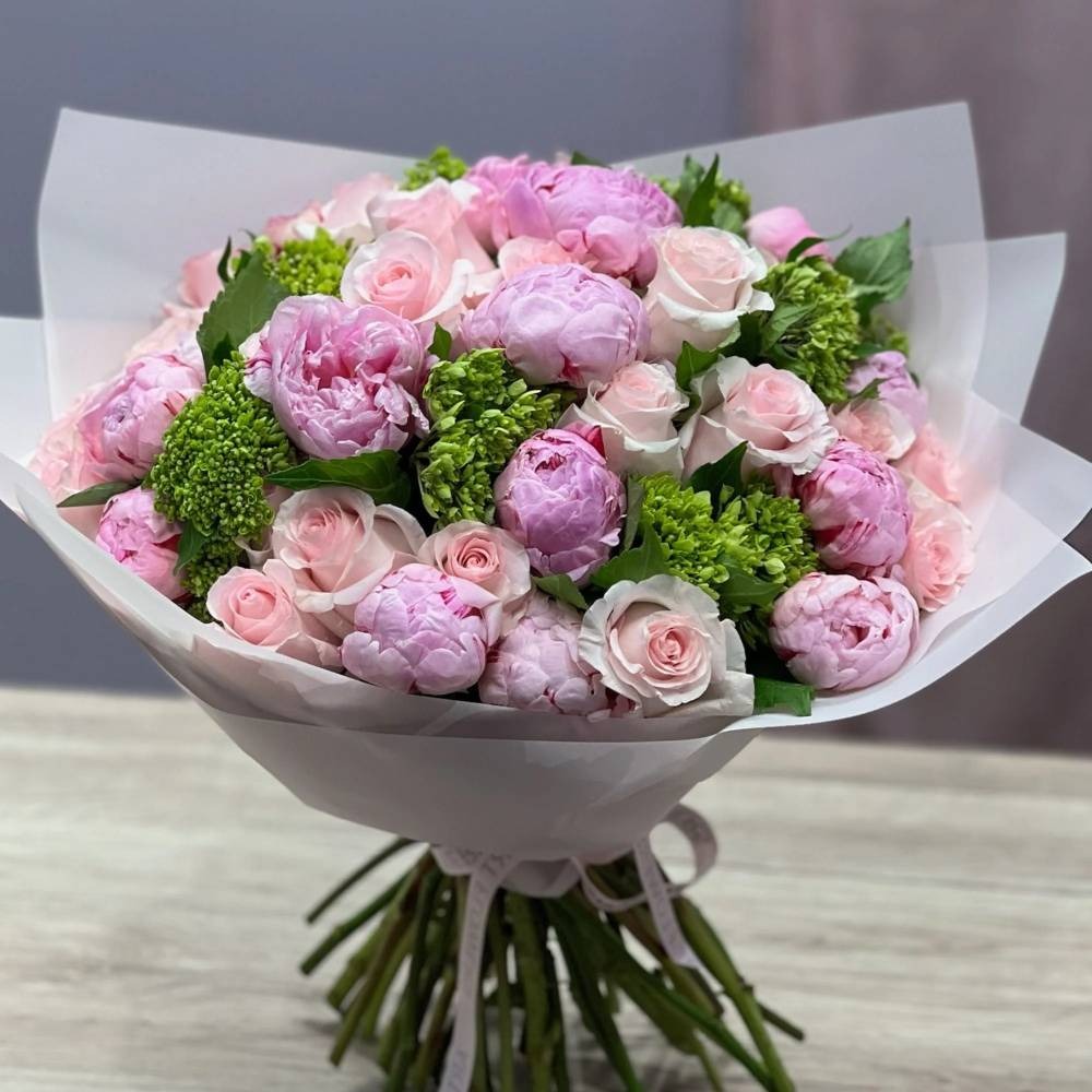 Bouquet of pink and green flowers wrapped in white paper on a light surface.