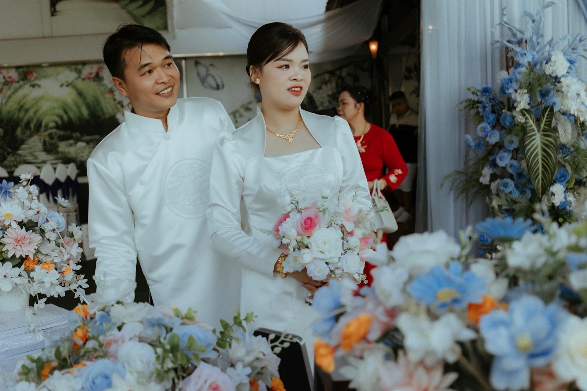 Couple in formal attire standing amidst floral decorations, likely at a wedding.