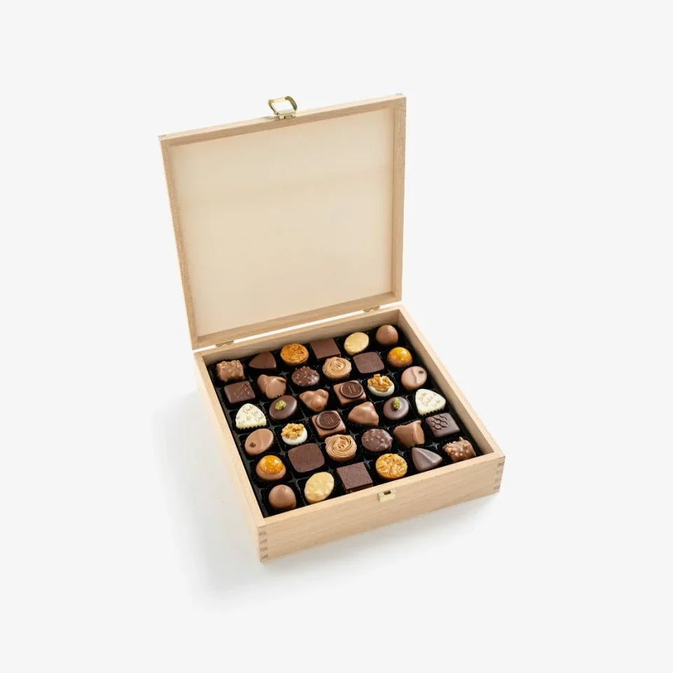 Open wooden box filled with assorted chocolates on a white background