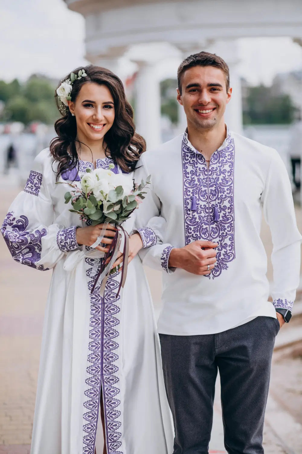 Couple in traditional embroidered outfits standing outdoors.