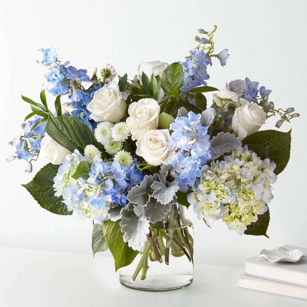 Bouquet of blue, white, and green flowers in a clear vase on a white background