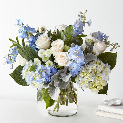 Bouquet of blue, white, and green flowers in a clear vase on a white background