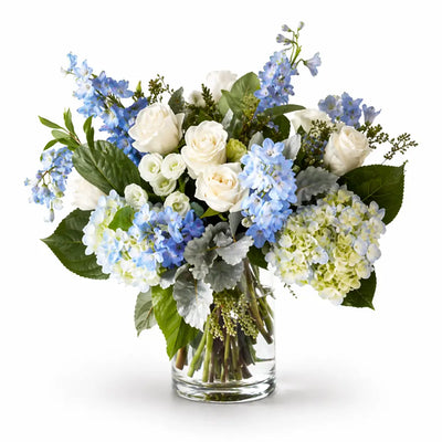 Bouquet of white and blue flowers in a clear vase on a white background
