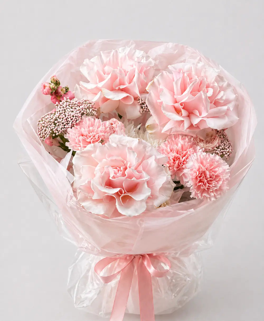 Bouquet of pink flowers wrapped in clear plastic with a pink ribbon on a light gray background