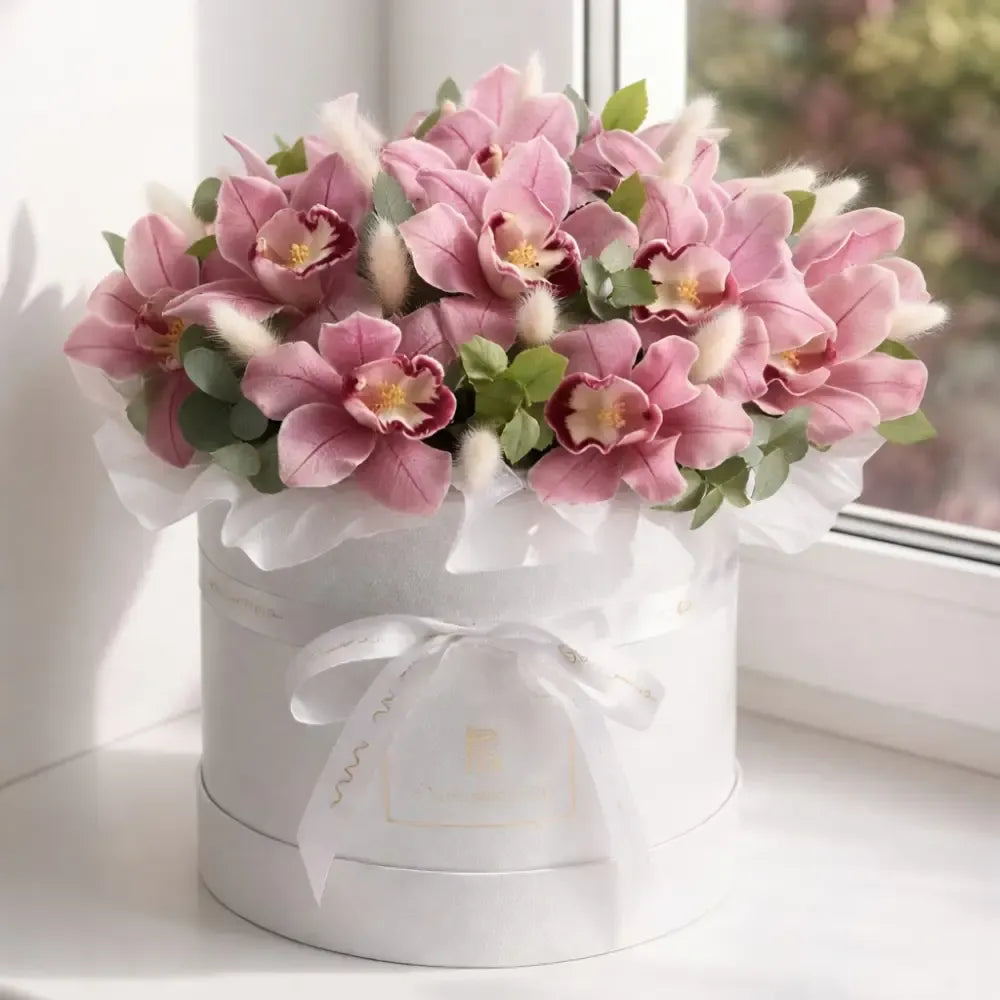 Pink flowers in a white box with a ribbon on a light surface.