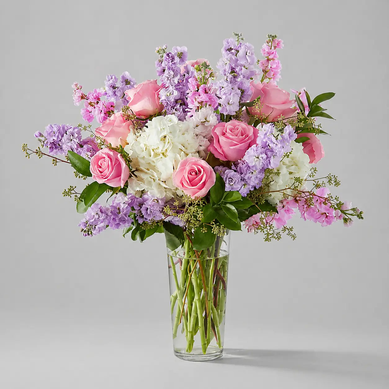 Bouquet of pink, white, and purple flowers in a clear vase on a gray background