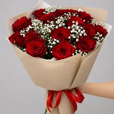 Bouquet of red roses with a red ribbon held by a hand on a gray background