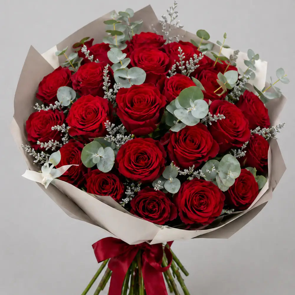 Bouquet of red roses with greenery and a red ribbon on a light gray background