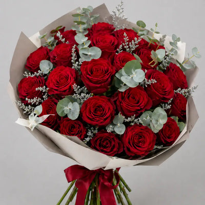Bouquet of red roses with greenery and a red ribbon on a light gray background