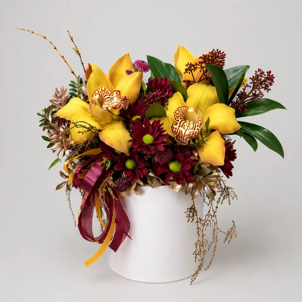 Bouquet of yellow orchids and red flowers in a white vase on a light gray background