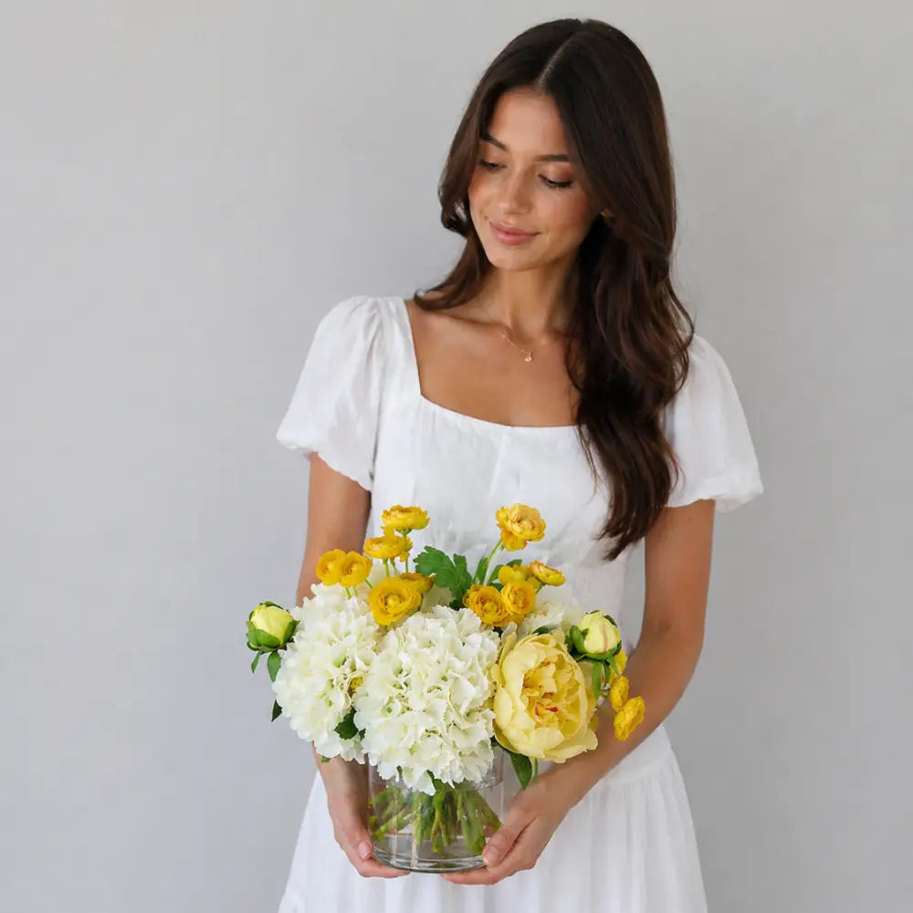 Woman holding a bouquet of yellow and white flowers against a gray background