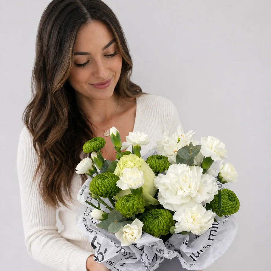 Woman holding a bouquet of white and green flowers against a plain background
