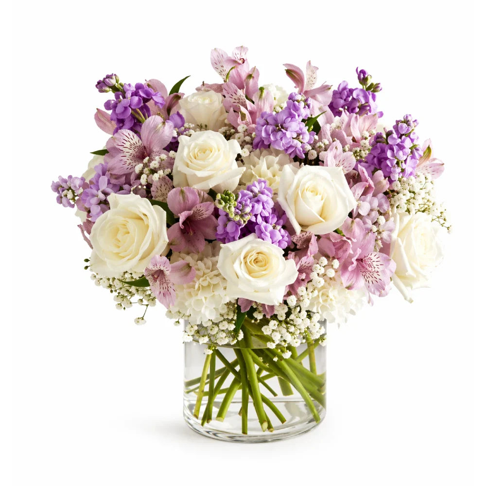 Bouquet of purple, white, and pink flowers in a clear vase on a white background