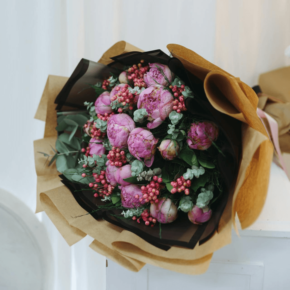 Bouquet of pink flowers with green leaves and red berries wrapped in brown paper on a white background