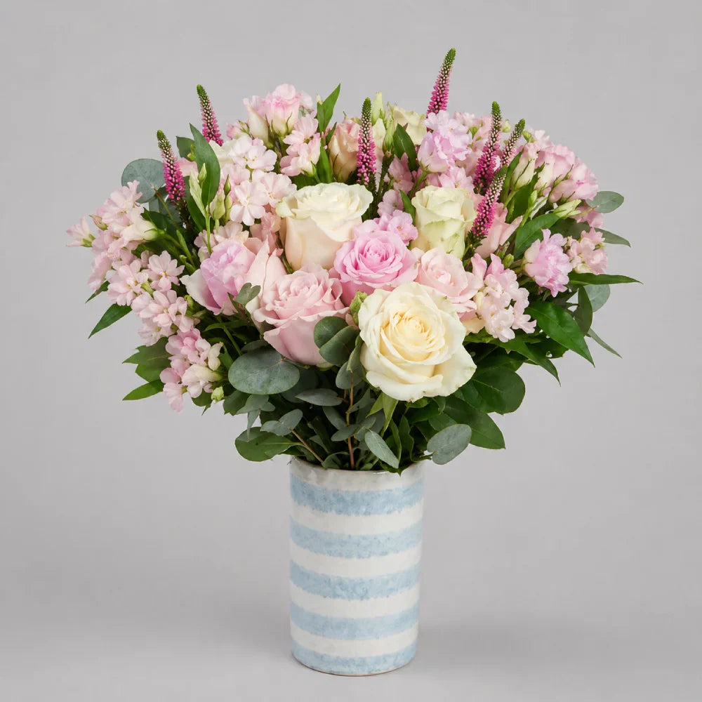 Bouquet of pink and white flowers in a striped vase on a gray background