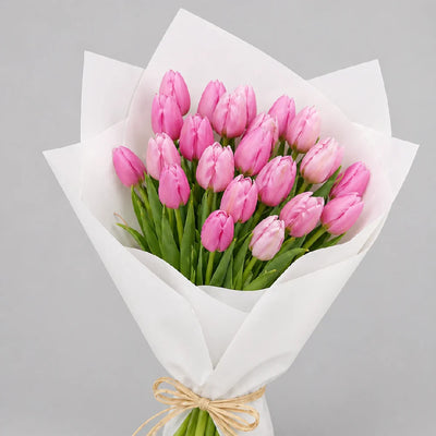 Bouquet of pink tulips wrapped in white paper with a beige ribbon on a gray background