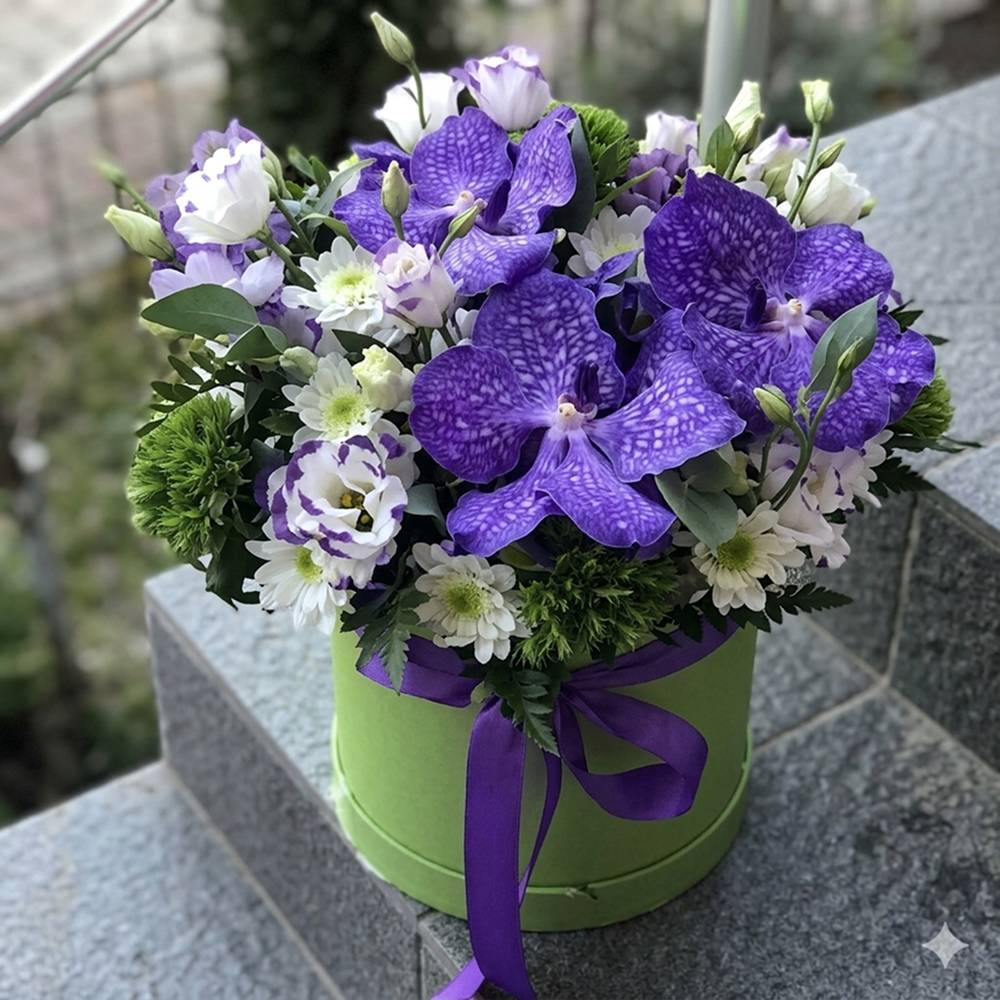 Bouquet of purple and white flowers in a green box with a purple ribbon on a stone surface.
