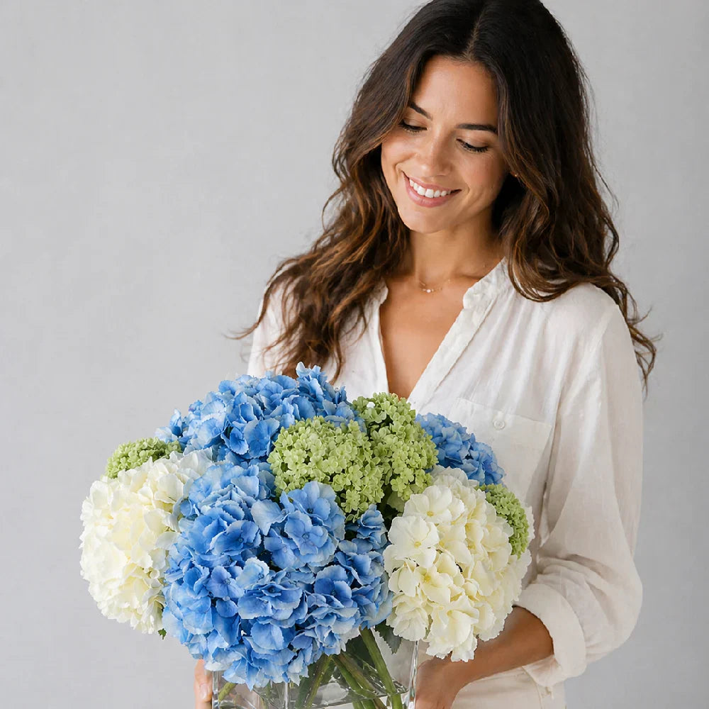 Woman holding a bouquet of blue, white, and green flowers against a gray background