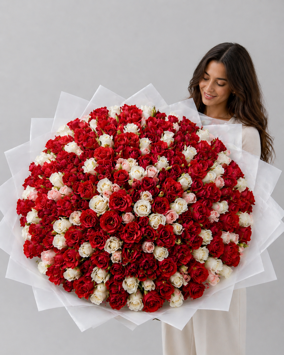 Woman holding a large bouquet of red and white flowers against a gray background