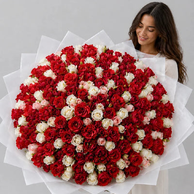 Woman holding a large bouquet of red and white flowers on a gray background