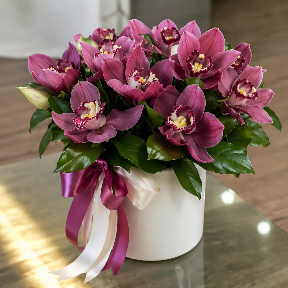 Bouquet of pink orchids in a white vase with ribbons on a reflective surface.