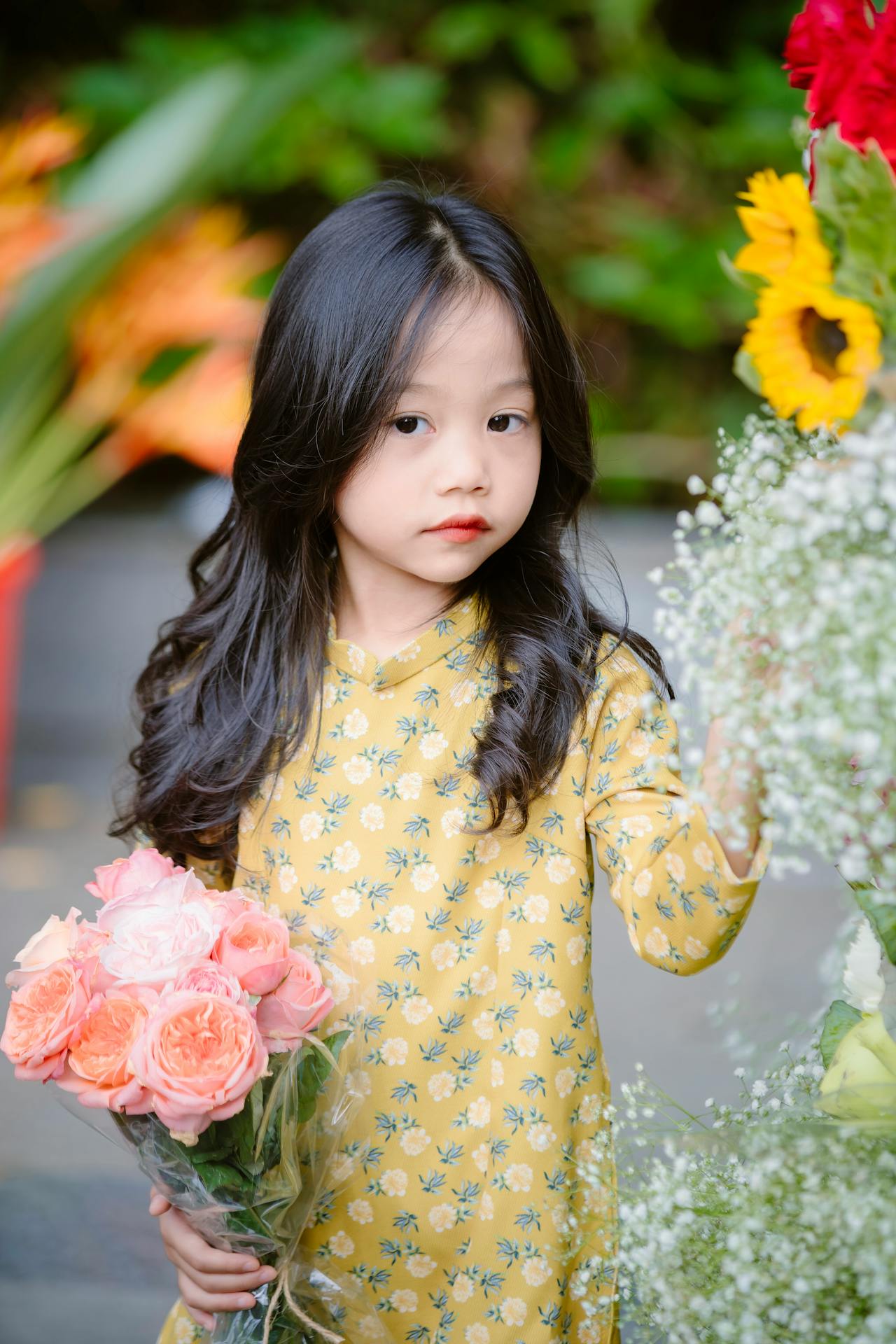 Young girl in a yellow floral dress holding flowers with blurred floral background